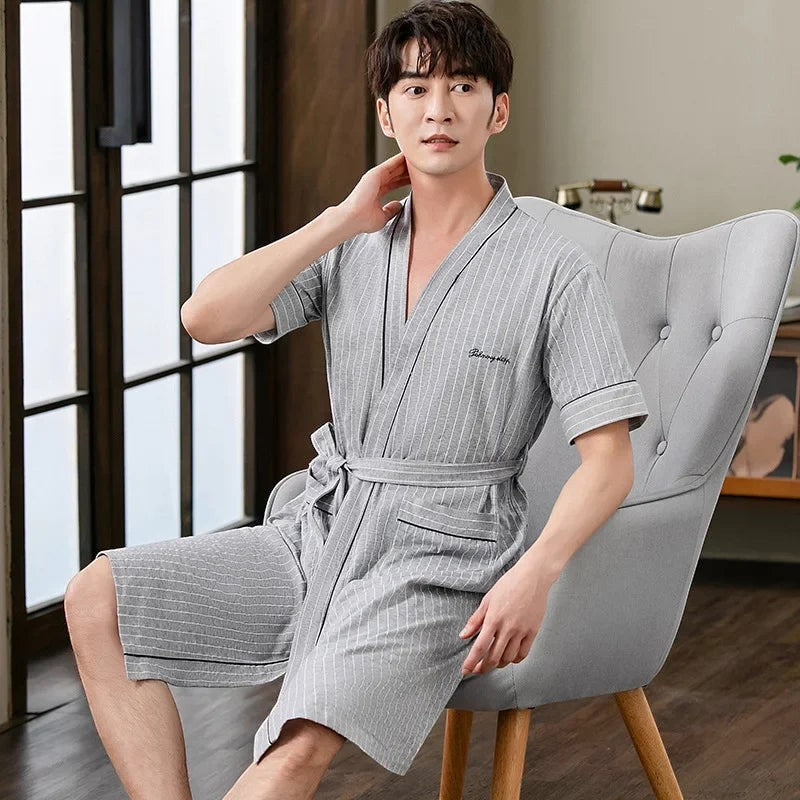 Homme portant un peignoir UnPeignoir gris à rayures blanches avec manches courtes, assis sur un fauteuil élégant.